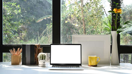 Front view computer laptop, picture frame, flower pot and stationery on white table.の写真素材