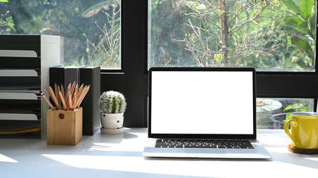 Comfortable workplace with laptop computer, stationery and coffee cup on white table.