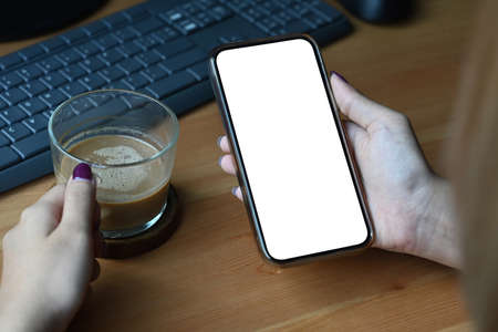 Woman holding cup of coffee and reading news on mobile phone. Blank screen for graphics display montage.の写真素材