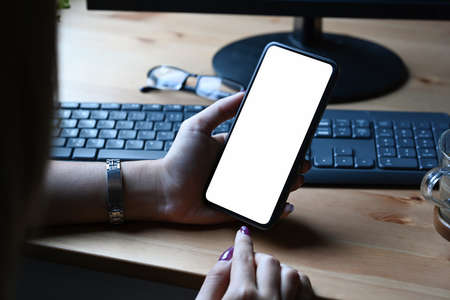 Woman holding cup of coffee and reading news on mobile phone. Blank screen for graphics display montage.の写真素材