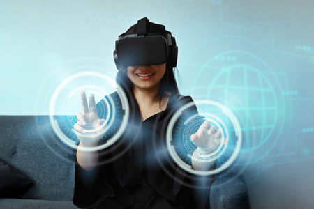 Smiling young woman wearing virtual reality handset and touching virtual screen in the foreground.