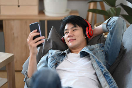 Happy asian male resting on couch and using smart phone.の写真素材