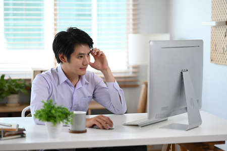 Pleased young businessman drinking coffee and checking financial data on digital tablet.