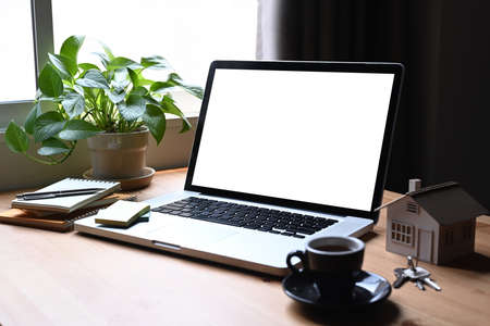 Mockup laptop computer, house model and keys on wooden table. Mortgage and real estate investment...