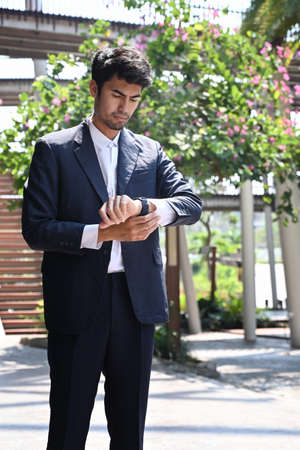 Elegant businessman checking time on his wrist watch while standing on city street.の写真素材