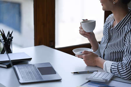 Pleased woman holding cup with hot beverage and looking through a window.の写真素材