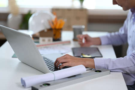 Close up view male architect using digital tablet and working blueprint at office desk. Architecture...