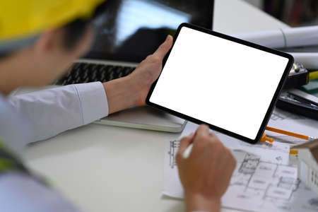 Close up view male architect using digital tablet and working blueprint at office desk. Architecture design concept.の写真素材