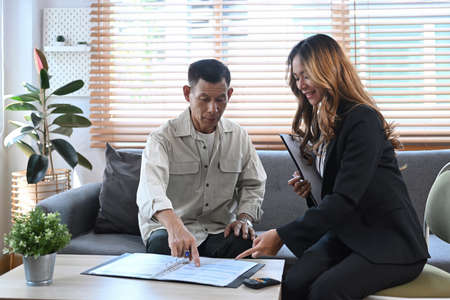 Smiling female agent holding digital tablet and explaining offer life insurance to elderly man. Senior health insurance concept.の写真素材