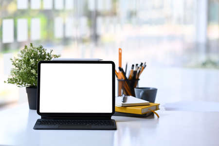 Mockup digital tablet with wireless keyboard, potted plant and stationery on white office desk.