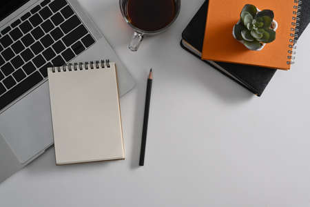 Top view empty notepad, laptop computer and coffee cup on white table. Flat lay.
