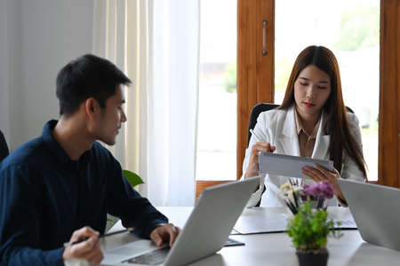 Two young entrepreneurs discussing project ideas, marketing strategy together at modern office.
