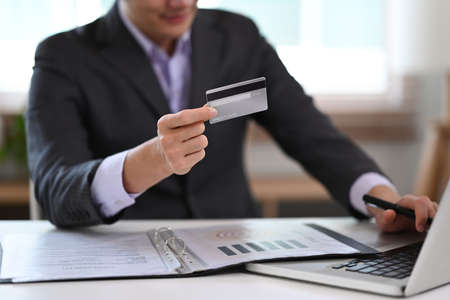 Young businessman holding credit card and using internet banking service on laptop computer.
