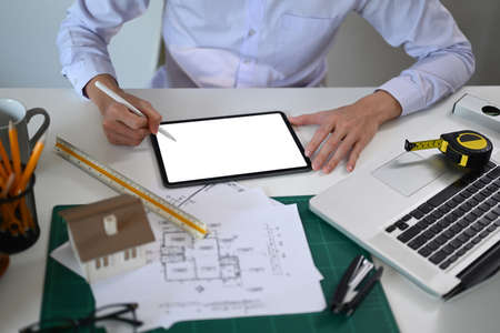 Cropped image of architect man using digital tablet and working with construction plans at office.の写真素材