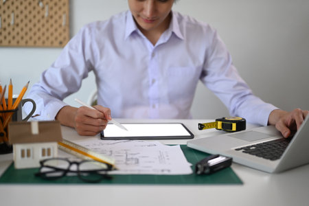 Close up view male engineer using digital tablet while working on architectural project at office.の写真素材