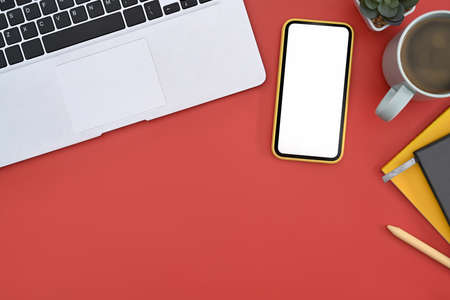 Smart phone with empty screen, laptop, notebook and coffee cup on red background. Top view.の写真素材