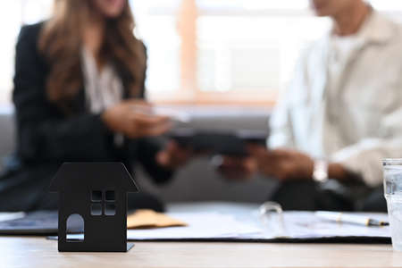 House model on wooden table and  financial adviser consulting contract mortgage loan with elderly man in background.の写真素材