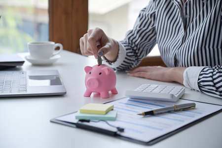 Woman hand putting coin into piggy bank. Saving money, banking, economy concept.の写真素材
