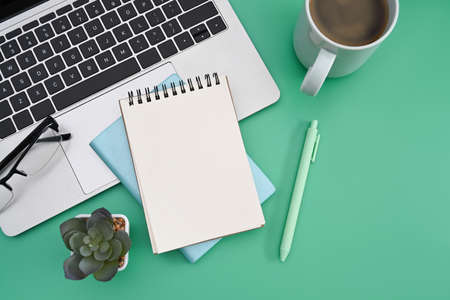 Top view notepad, laptop computer, coffee cup and cactus on green background.