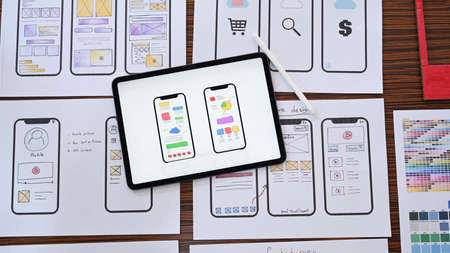Web designer workplace with digital tablet and wireframe sketches of screens for mobile application.