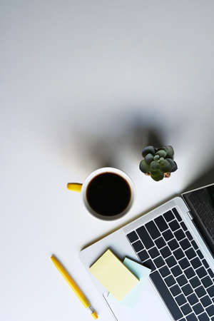 Simple workplace with computer laptop, coffee cup, notebook and succulent plant on white table.の写真素材