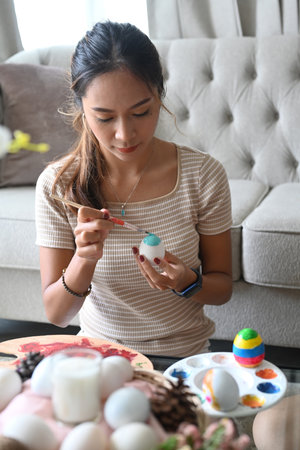 Attractive young woman sitting in living room and painting egg for Easter festivity.の写真素材