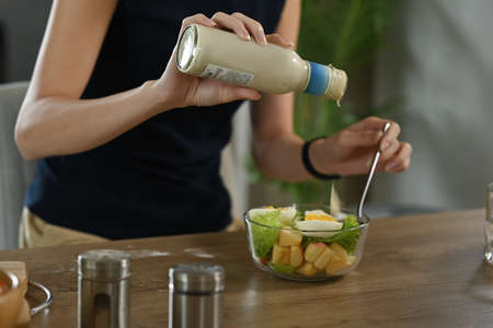 Young woman pouring sauce from bottle into healthy vegetable salad. Diet and Healthy food concept.の写真素材