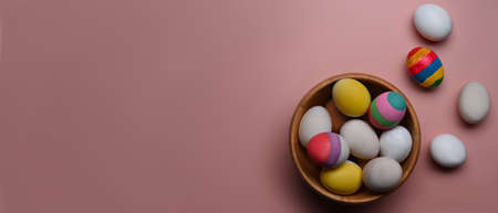 A wooden bowl full of Easter eggs on pink background with copy space for text or design.の写真素材