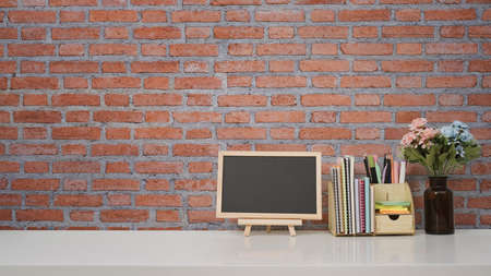 Blank small blackboard and supplies on white table against brick wall with copy space for your text message or product isolated.の写真素材