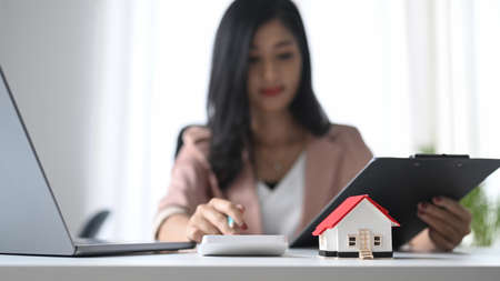 Small house model on white table and professional financial advisor is using calculator.の写真素材