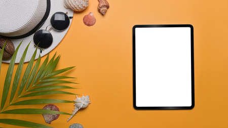 Digital tablet, traveler accessories, seashells and tropical palm leaves on yellow background....