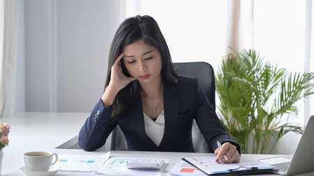 Stressed female office worker looking worried, tired and overwhelmed while working at office desk.