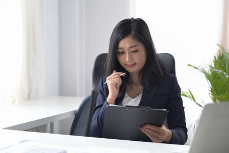 Millennial businesswoman sitting in bright office and reading financial reports.の写真素材