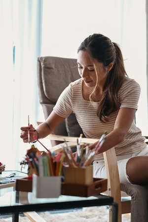 Attractive millennial woman in casual clothes sitting in bright living room and enjoy creating her artwork.の写真素材