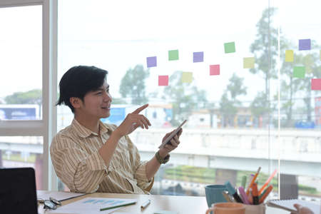 Handsome asian businessman sitting at creative workplace and using digital tablet.の写真素材