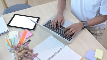 Cropped shot male office worker using laptop computer on wooden table.