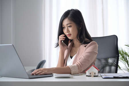 Millennial young woman sitting at comfortable workplace and talking on mobile phone.