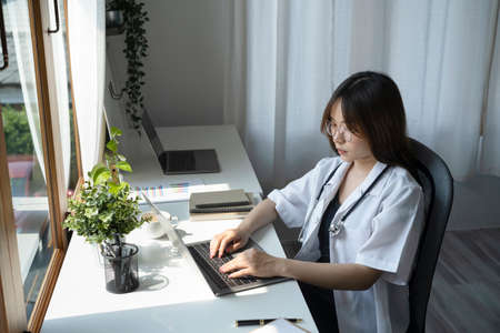 Side view female doctor in white uniform using laptop computer at medical office.の写真素材