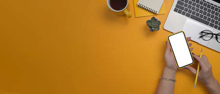 Overhead shot of stylish woman using mobile phone over yellow background.