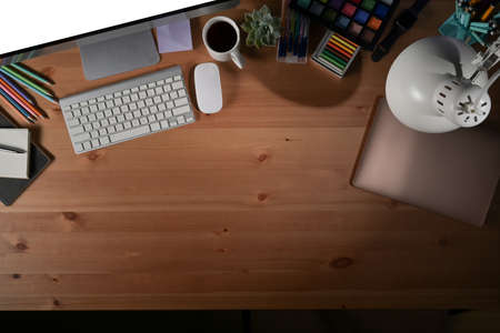 Above view creative designer workplace with computer, coffee cup and stationery on wooden table.