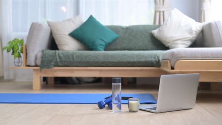 Equipment for training at home. Dumbbells, laptop, bottle of water and yoga mat on wooden floor.の写真素材