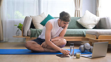 Handsome man watching fitness lessons online on laptop, exercises at home.の写真素材