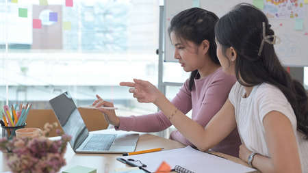 Two young creative women are working, discussing ideas for new strategy of development together.