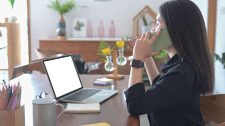 Portrait of young asian woman sitting in bright modern office and making notes on document.の写真素材