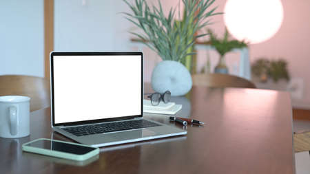Computer laptop with white screen, smart phone and glasses on wooden office desk.