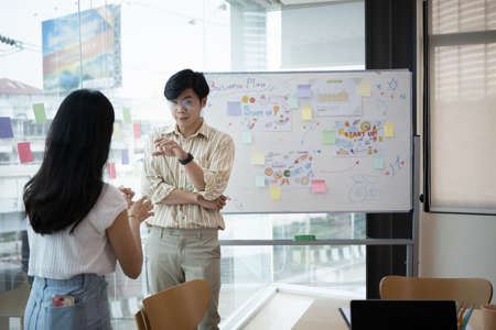Two start up business people in having a discussion while standing by windows in office overlooking...