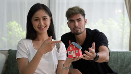 Happy young couple holding house model and smiling to camera. New house, insurance and real estate...