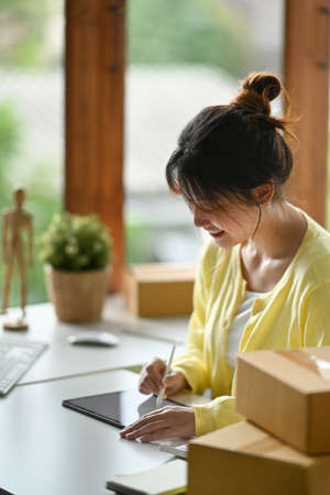 Woman online seller using digital tablet for confirming orders or taking orders from customer.の写真素材