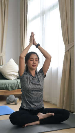 Healthy young woman sitting in lotus position on mat in living room. Healthy lifestyle concept.の写真素材