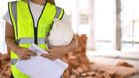 unrecognized architect with blueprint in hand and helmet standing at construction site Industry,...